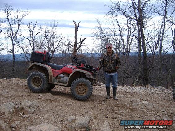 Red ATV with storage box, side view. Person standing next to it