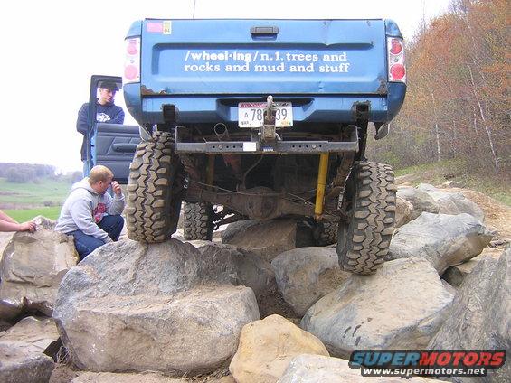 Blue pickup truck with large tires on rocks, people watching
