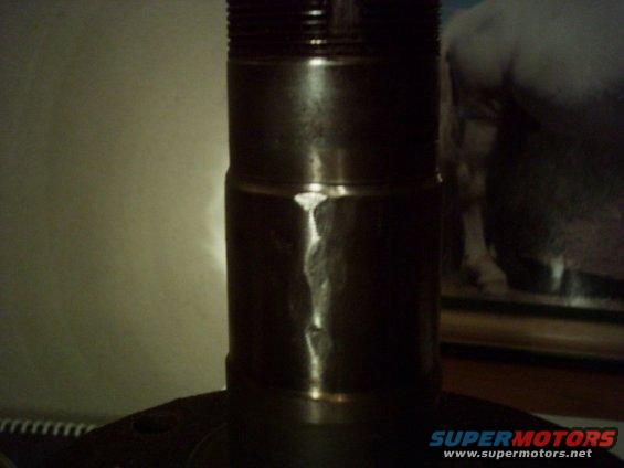 Close-up of a metal part with a threaded section at the top and a visible seam
