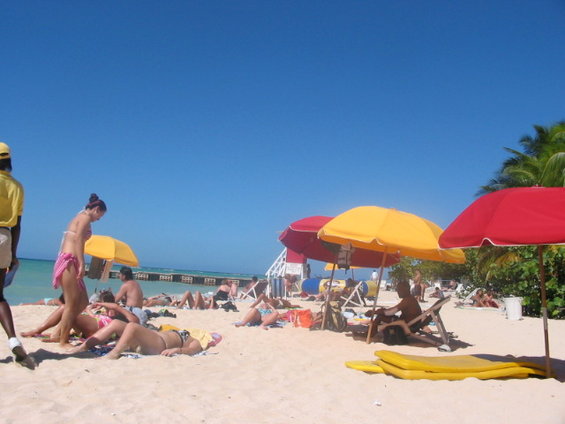 People relaxing on a sandy beach under umbrellas with a clear blue sky