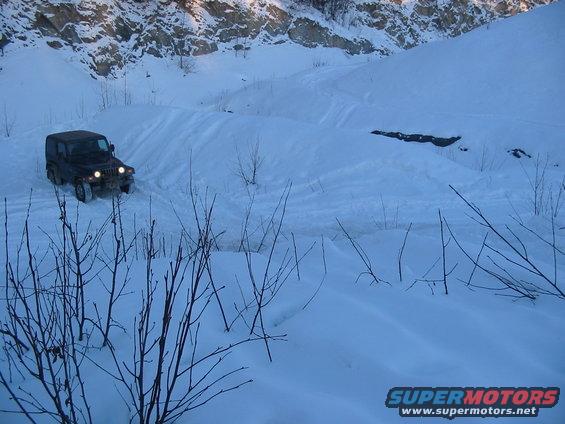 Dark green Jeep Wrangler TJ driving on a snowy mountain road, front-left view