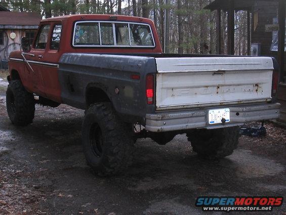 Lifted pickup truck, red cab, dark gray bed, white tailgate. Big off-road tires