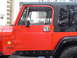 1989 Jeep YJ - The side profile of a red 1989 Jeep YJ shows its distinctive door and fender design.