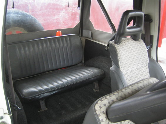 1987 Suzuki Samurai interior showing rear bench seat, spare tire behind window, and front seats