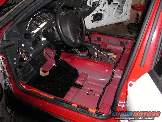 Red car interior with dashboard removed, showing exposed wiring and bare floor panels