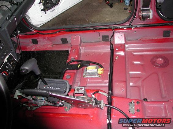 Interior of a car with seats and carpet removed, showing the floor pan, shifter, and wiring
