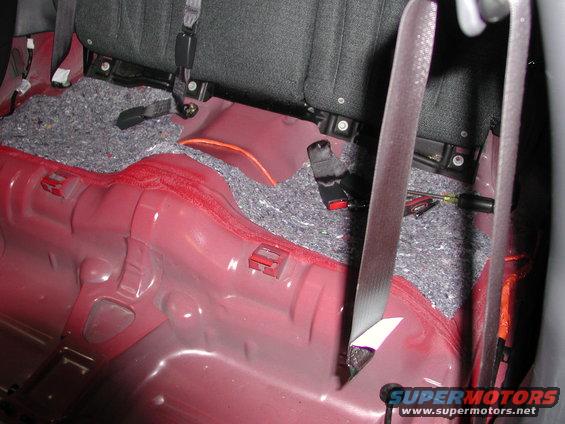 Rear floor of a car with seats removed, showing red metal and sound deadening material. Seatbelts are visible
