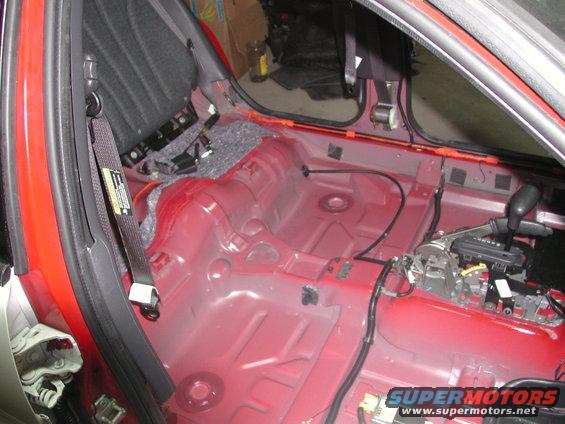 Red interior floor and rear seat area of a car with removed upholstery and carpeting. Gear shifter visible