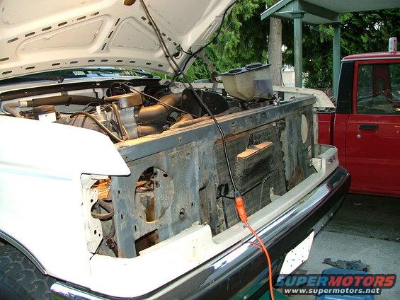 1988 Ford Bronco engine bay with hood open, radiator removed, and a red truck in the background
