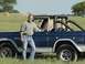 1974 Ford Bronco - A man poses with a blue 1974 Ford Bronco in a grassy field with hay bales in the background.