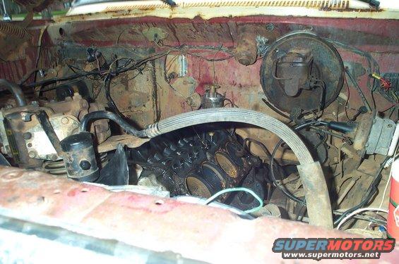 Engine bay with exposed cylinder heads, hoses, and wiring. Red and rusty metal