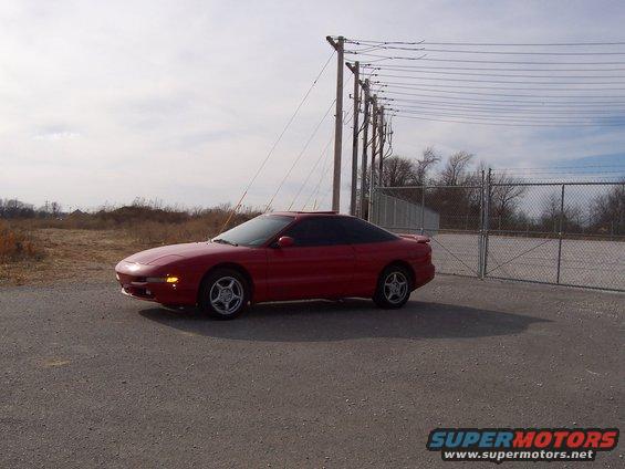 Red 1996 Ford Probe parked on asphalt near a chain-link fence and utility poles