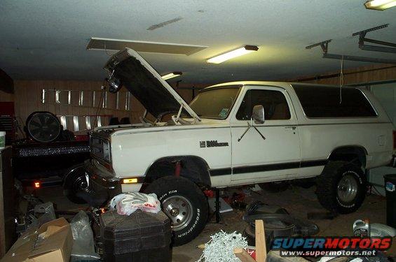 White Dodge Ramcharger SUV with hood open, lifted suspension, and off-road tires in a garage