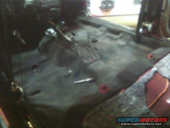 Car interior with carpet removed, showing floor pan and some wiring
