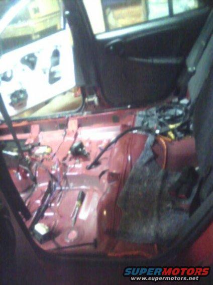Red car interior with door panel removed, showing exposed wiring and red painted metal floor
