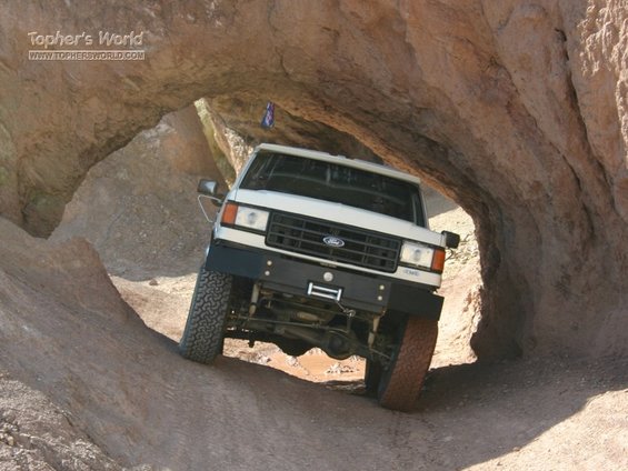 White 1988 Ford Bronco navigating a narrow rock tunnel