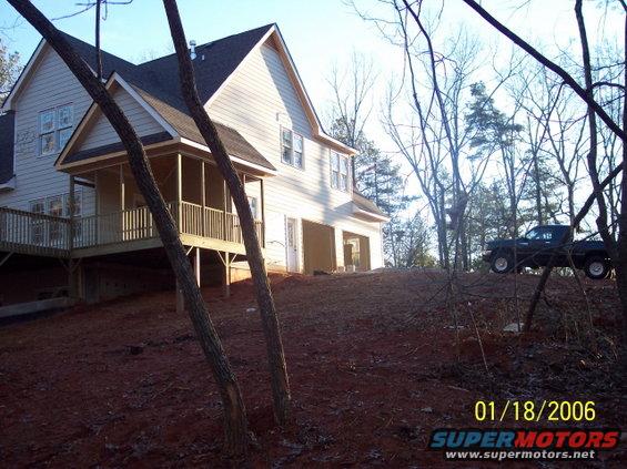 Dark pickup truck parked on a dirt hill next to a house under construction