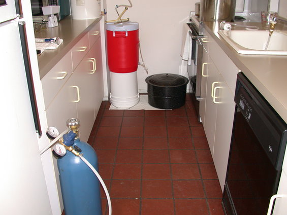 Brewing equipment in a kitchen with a blue gas tank and red cooler