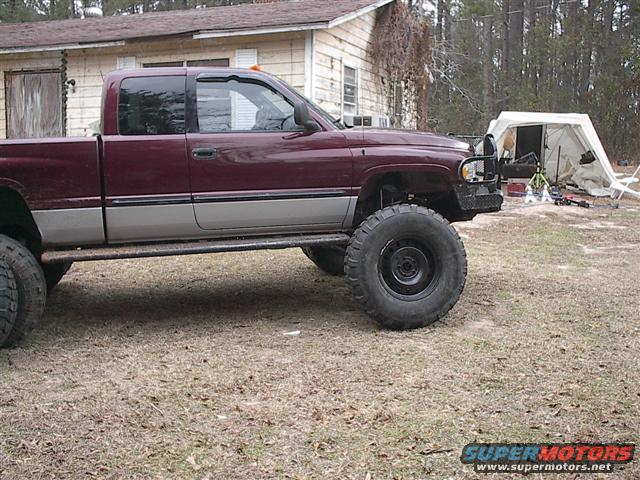 Maroon and gray lifted pickup truck parked in a yard with a tent in the background