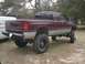 2001 Dodge 1500 - This maroon 2001 Dodge 1500 pickup truck is shown from the rear 3/4 angle, a lifted suspension and oversized tires.