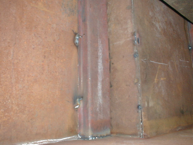 Close-up of a vehicle's metal floor pan with some rust and what looks like a seam