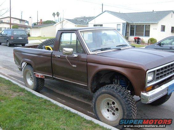 Brown pickup truck with lifted suspension and off-road tires parked on a curb
