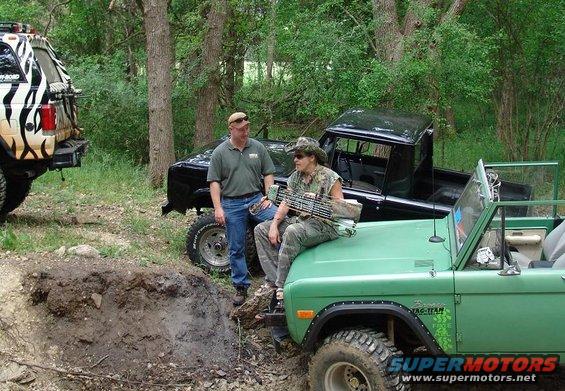 1978 Ford Bronco and a black pickup truck parked off-road with two people