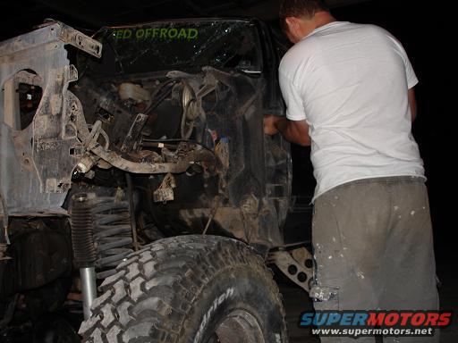 man working on heavily damaged off-road vehicle, large tire visible