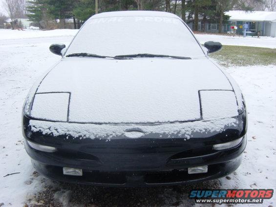 Black Ford Probe covered in snow, front view. Pop-up headlights are visible