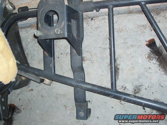 Close-up of a black metal frame part, possibly from a seat assembly, with a beige cushion visible on the left
