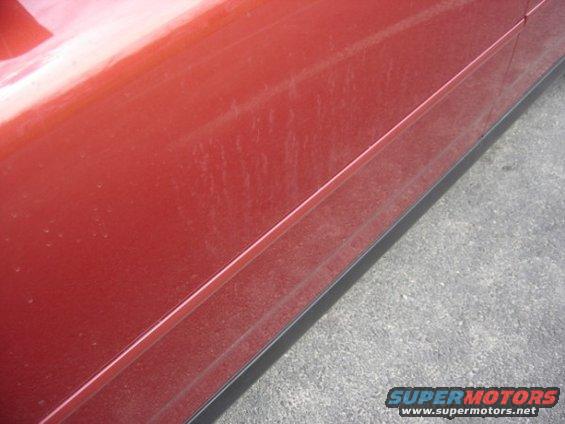 Close-up of a dusty red car door panel with a black trim piece along the bottom