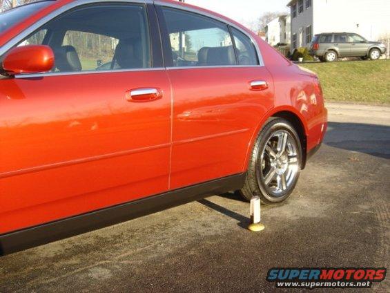 Red sedan with chrome wheels, jacked up on a yellow and white chock, side view