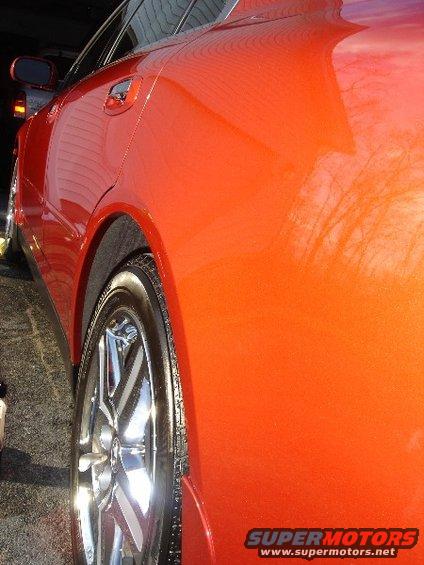 Orange sedan rear quarter panel, wheel, and door handle. Water spots visible on paint