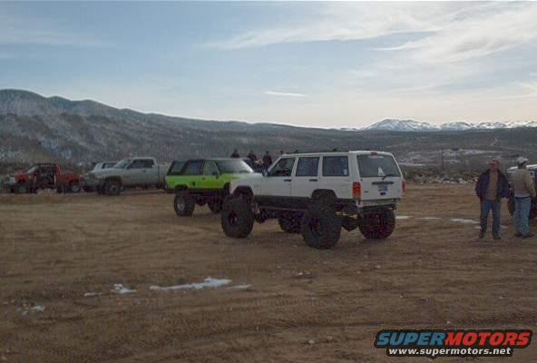 Several lifted off-road vehicles parked on a dirt lot with mountains in the background