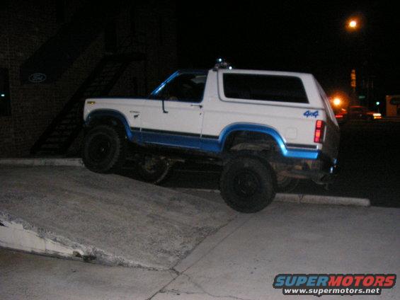 White and blue Ford Bronco with 4x4 badging parked on a ramp at night