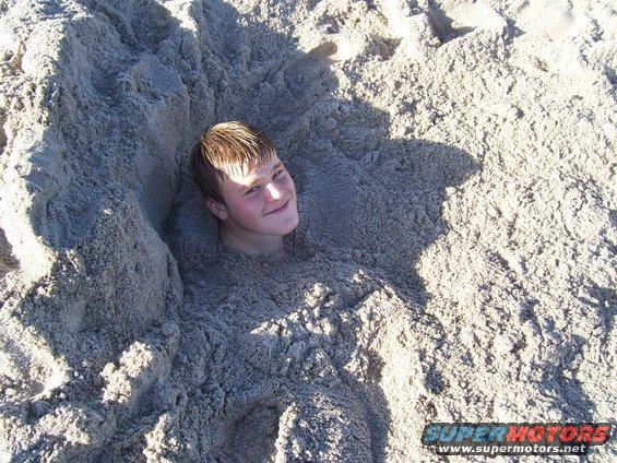 Person buried up to their head in sand on a beach, smiling