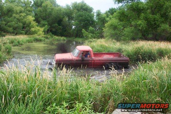 Red pickup truck stuck in muddy water, side view. The truck is partially submerged