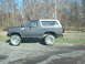 1986 Ford Bronco - This lifted Ford Bronco sits on a gravel surface with a wooded area in the background.