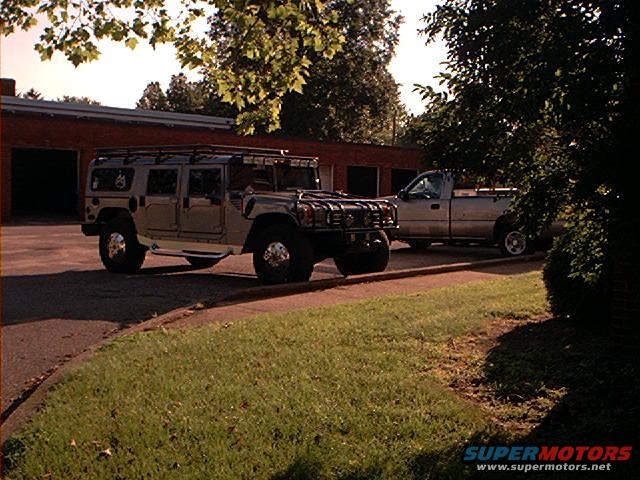 Hummer H1 parked next to a silver pickup truck in front of a brick building