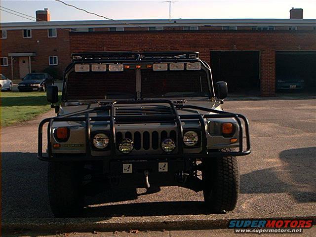 Gray Hummer H1 with a roof rack, brush guard, and multiple lights