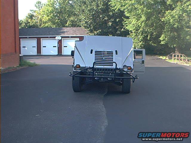 Rear view of a light-colored Humvee parked in front of a garage