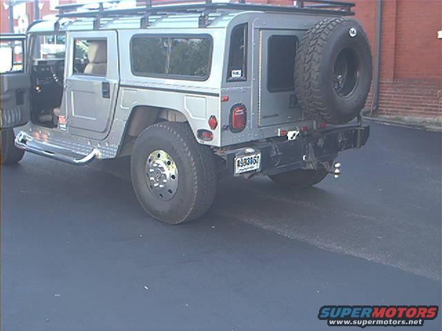 Silver Hummer H1 with a spare tire mounted on the rear, seen from the rear-right