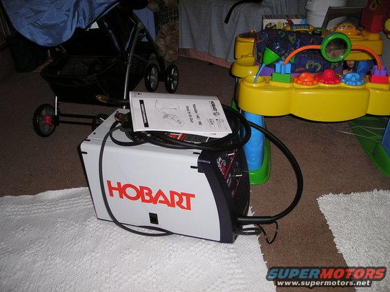 Hobart welder on floor next to a baby stroller and a toy