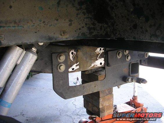Close-up of truck frame showing suspension and hitch receiver, supported by blocks and a jack