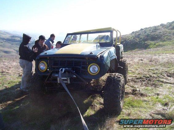 Off-road vehicle with winch and yellow roll cage, people gathered around the front