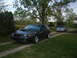 1999 Ford Mustang - Two Ford Mustangs are parked in a driveway on a cloudy day, with trees and a house visible.