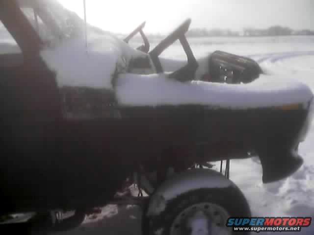 Dark vehicle with snow on hood and roof, side view, with a wheel visible in snow