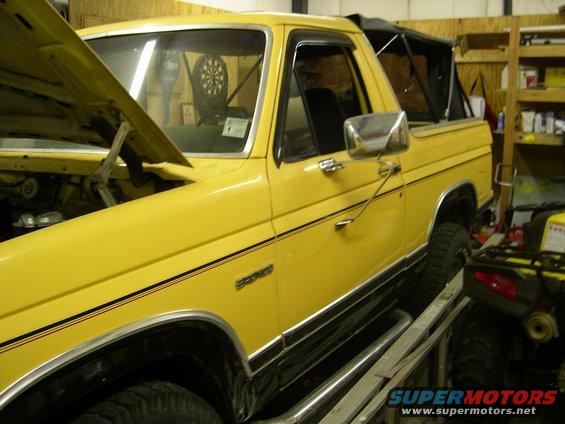 Yellow Ford Bronco with black trim and a soft top, hood open, on a ramp