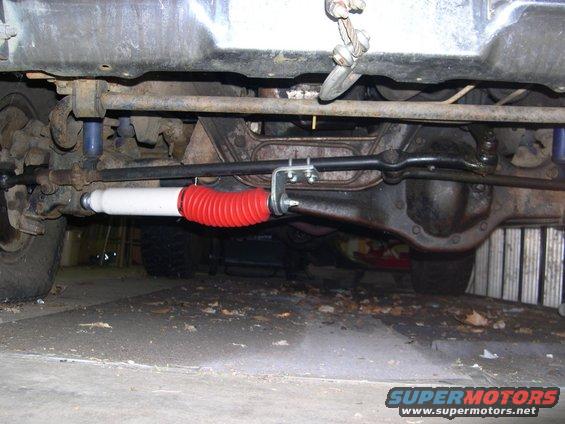 Underside of a vehicle showing the steering linkage and a shock absorber with a red bellows
