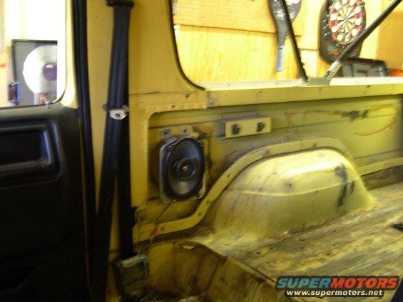 Interior shot of a yellow vehicle showing a speaker mounted on the side panel, a seatbelt, and the rear cargo area